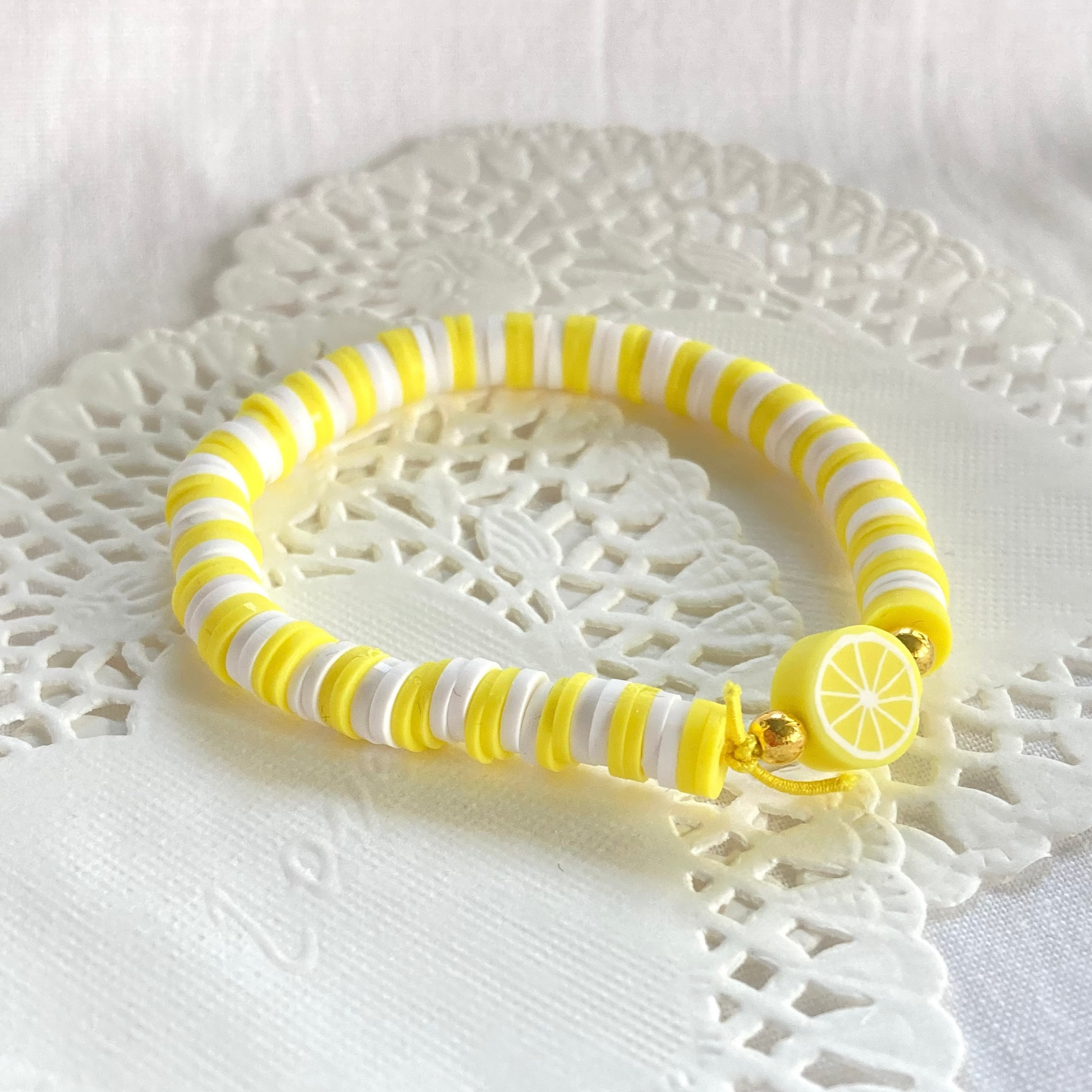 Yellow and white striped bracelet with a lemon charm on a white lace doily