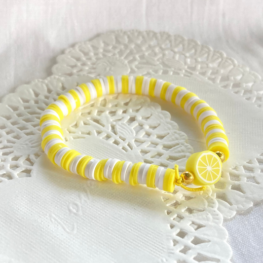 Yellow and white striped bracelet with a lemon charm on a white lace doily